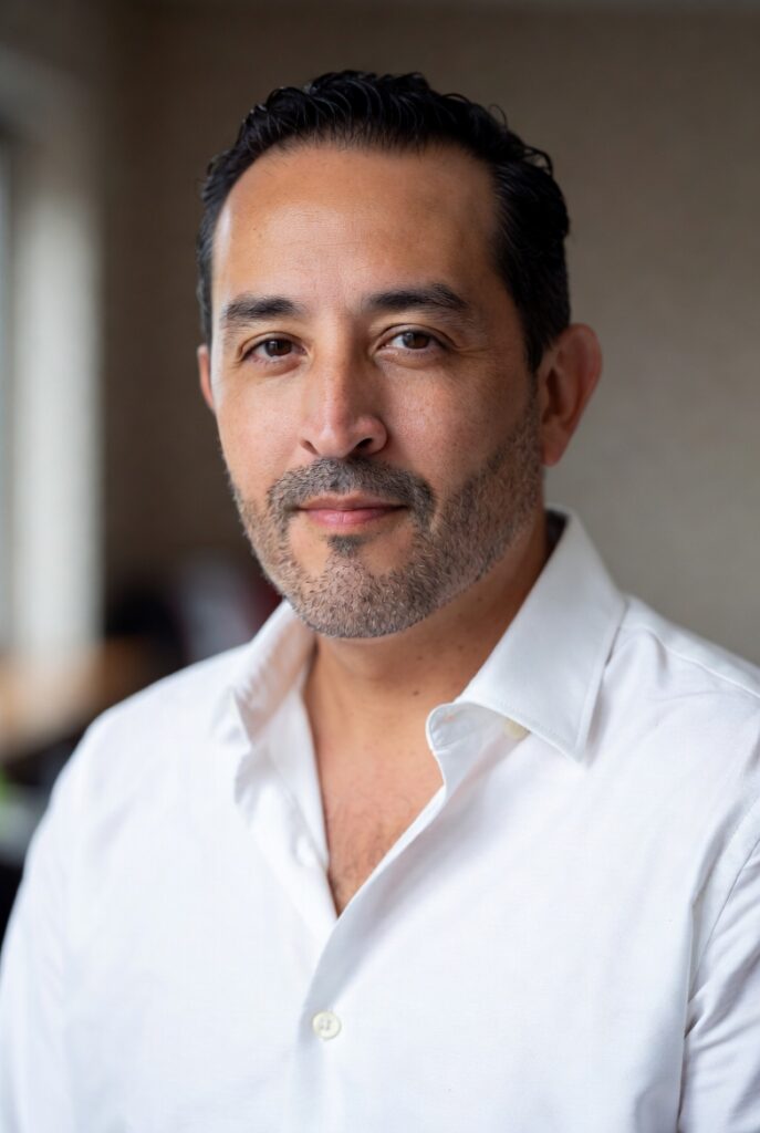 Professional editorial headshot portrait of a Latino man in his late 30s to early 40s